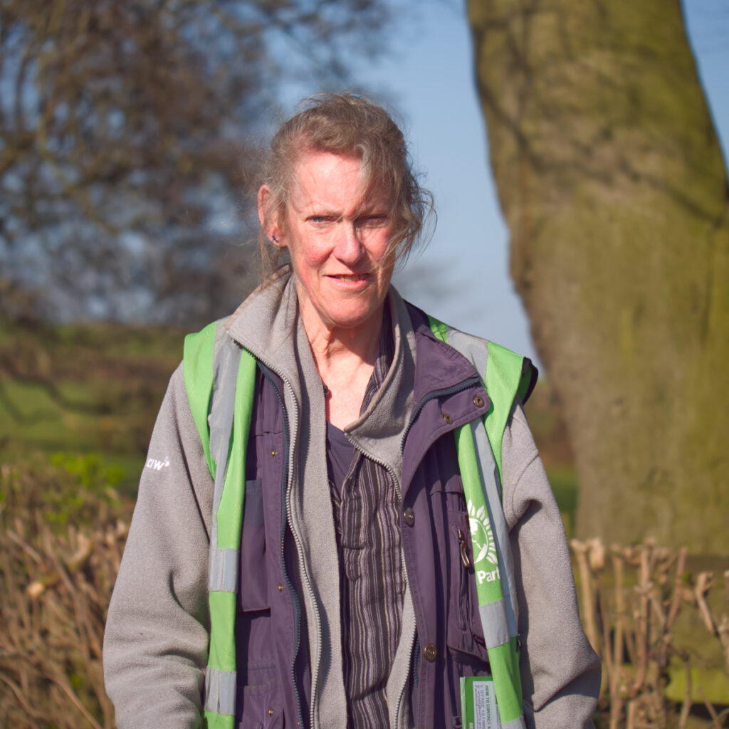 Alex Marsh in a fleece and Green Party-branded high-vis jacket stood next to a tree