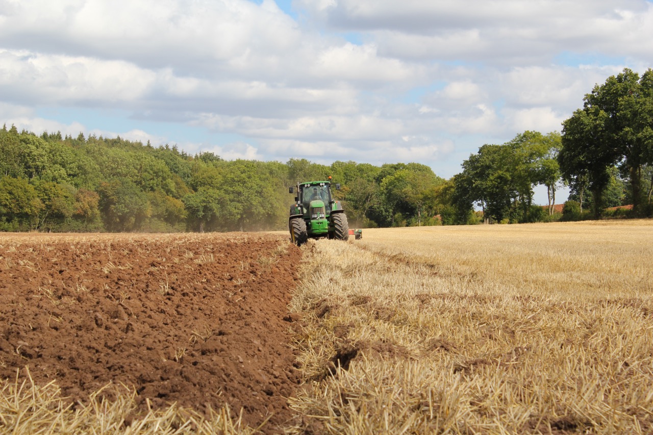 A farmer part-way through working their field in a green tractor.